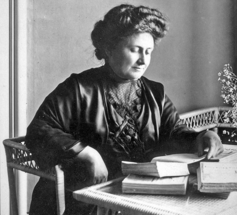 Schwarz-weiß Bild von Maria Montessori am Tisch beim lesen
