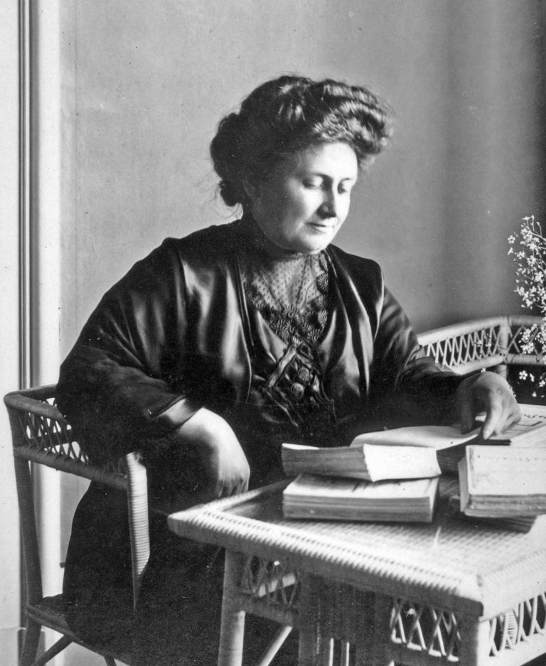 Schwarz-weiß Bild von Maria Montessori am Tisch beim lesen