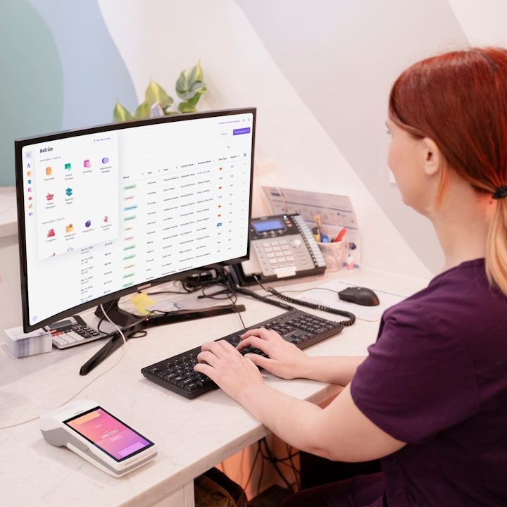 Frau arbeiten digital an einem Laptop und schreibt sich nebenher Notizen in einem Notizbuch auf