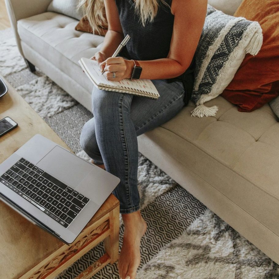 Frau arbeiten digital an einem Laptop und schreibt sich nebenher Notizen in einem Notizbuch auf