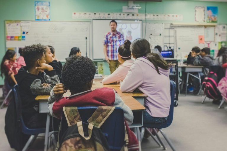 Lehrer im Unterricht in einer Klasse mit digitalen Medien im Hintergrund
