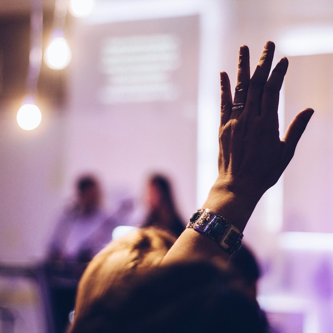 Person will eine Frage stellen und streckt den Arm nach oben